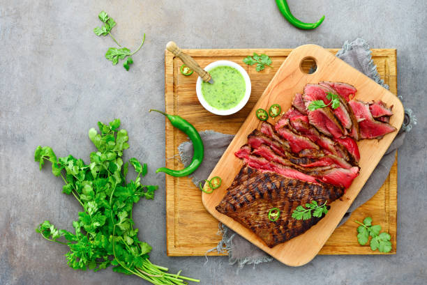 Flank steak on a wooden cutting board Flank steak ready to eat cut and served on a wooden cutting board with chimichurri sauce, overhead view flank steak stock pictures, royalty-free photos & images