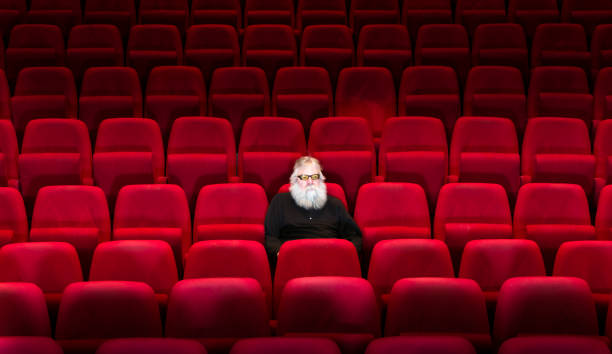 istock One man with white beard sits in Empty cinema or theatre with comfortable red seats 936167820