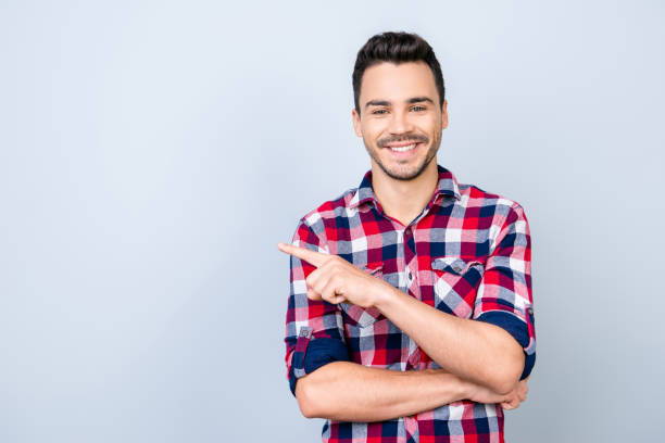 istock Advertising concept. Young successful smiling freelancer student on the pure light background in casual checkered outfit is pointing on a copyspace with his finger 936177296
