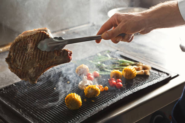 Unrecognizable male chef cooking medium beef steak and vegetables on grill. Healthy exclusive food prepared at professional kithen, closeup