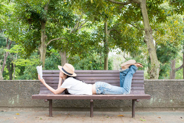Black hair woman is reading a book on a bench in the park
