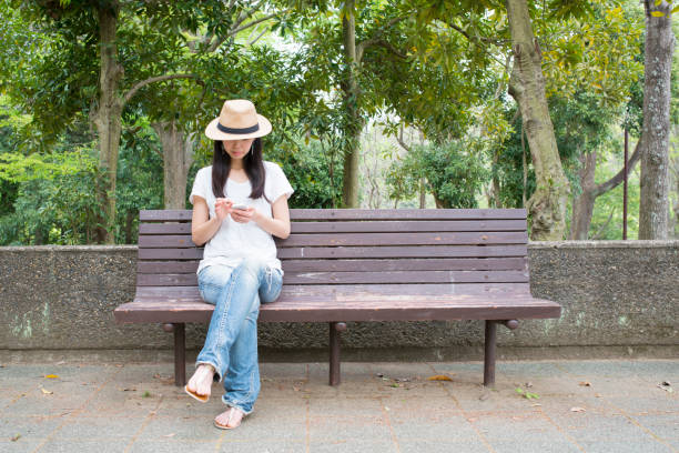 A woman is watching a smartphone at a park bench