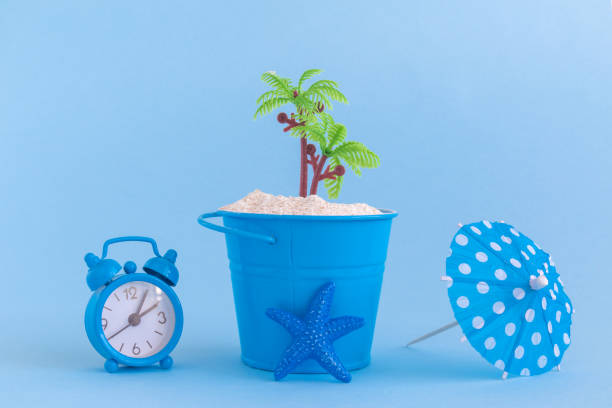 istock Starfish, paper cocktail parasol, can with sand and plastic palm tree isolated on blue background. Summertime vacation minimalistic still life concept. 936222228