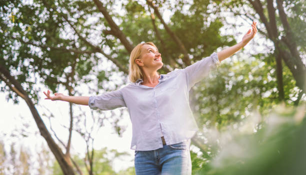 happy woman in spring or summer forest park open arms with happiness, hope and vitality. Caucasian girl relaxing and enjoying life on nature outdoors.