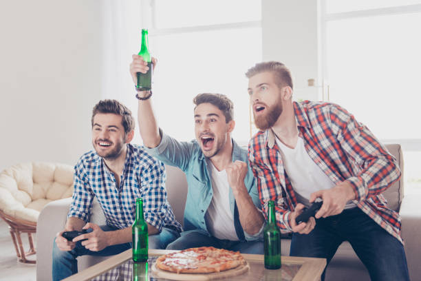 verrückt, funky, chill, freude, gewinner und verlierer! drei junge männer auf couch sitzen und spielen von videospielen drinnen zu hause mit bier und pizza, ausdruck von emotionen und gefühlen, gestik - winner looser stock-fotos und bilder