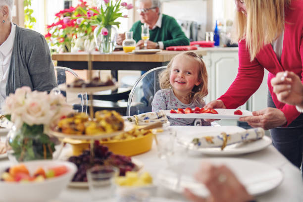 Child birthday party. Adorable little boy and girl with birthday cake decorated flowers and burn candle, makes wish. Kid in festive dress at room with balloons, bouquet of flowers at vase