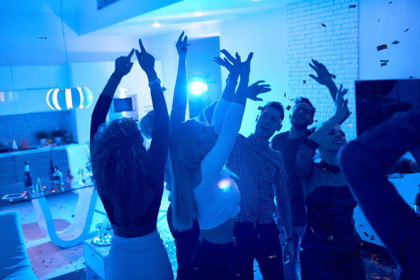 People enjoying House Party Group of modern young people dancing under confetti at private house party lit by blue light party stock pictures, royalty-free photos & images