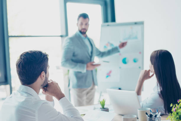 istock Focused rear view of three colleagues, concentrated on data at the flipchart, disscussing the solutions of their company`s problems and sharing opinions and ideas, in light modern workplace wearing smart clothes 936277128
