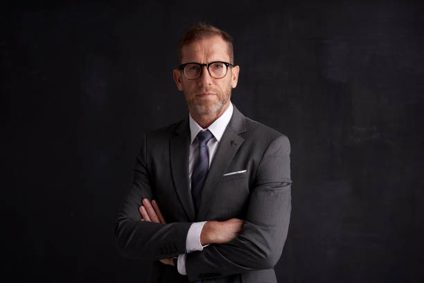 Executive senior businessman portrait Portrait of middle aged wrinkled businessman with arms crossed wearing suit while posing at dark background. necktie photos stock pictures, royalty-free photos & images
