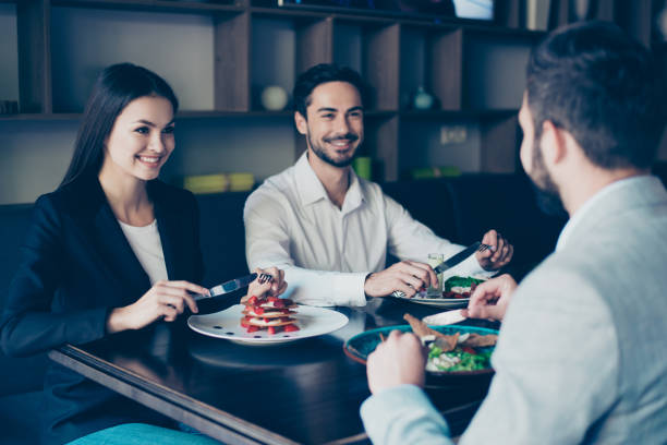 istock Three friendly buiseness colleagues in formal suits are sitting in restaurant and smiling, having nice and delicious treats, talking 936279250