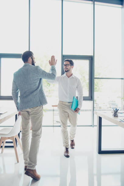 in voller größe von zwei hübschen brunet jungs kollegen, edel und elegant gekleidet, hohe fünf indem man einander im büro, erfolgreiche freundliche männer geben - business relationship white collar worker office glasses stock-fotos und bilder