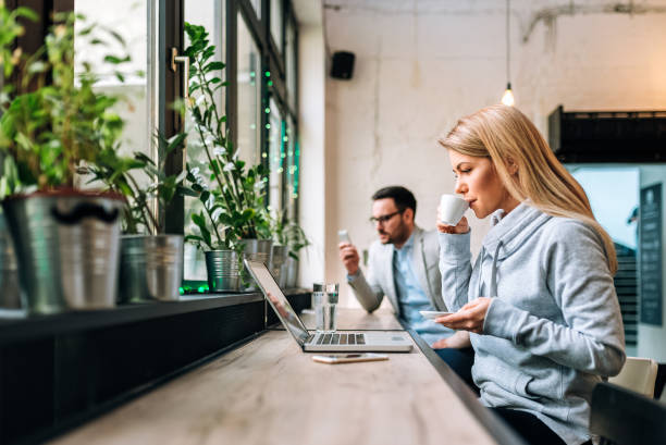 istock Writing post from cafe. Young woman drinking coffee while working on a laptop with handsome man at the background. 936283832