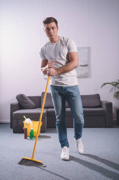 istock handsome man sweeping living room with broom and looking at camera 936296386