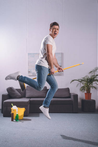 istock handsome man jumping with broom in living room 936297218