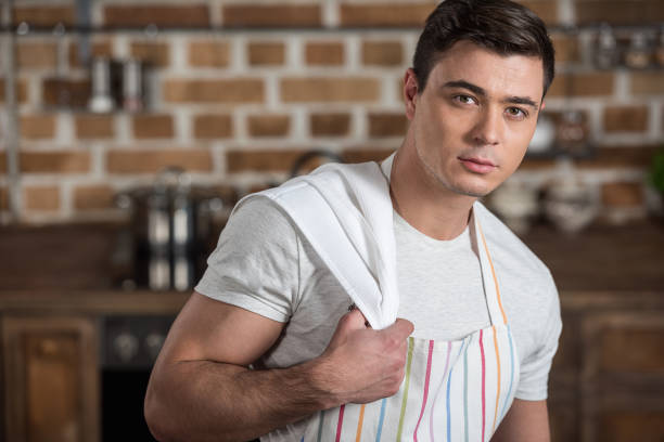 istock handsome man in apron with towel on shoulder looking at camera at kitchen 936297894