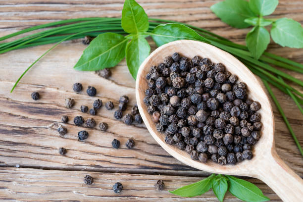 pepe nero in cucchiaio di legno su tavolo rustico con basilico fresco e cipolla verde - grano di pepe nero foto e immagini stock