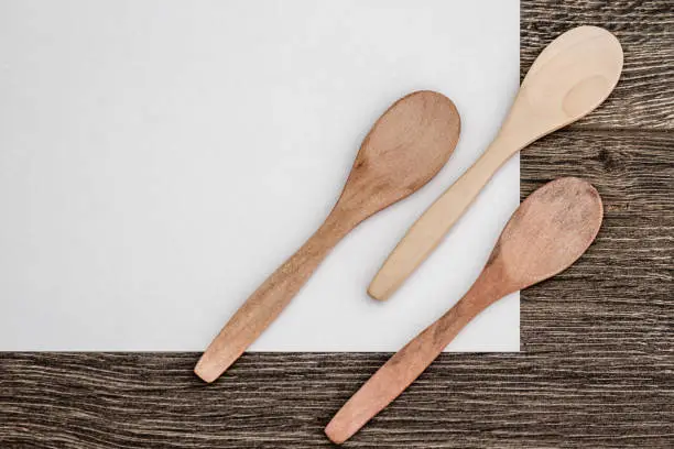 Wooden spoons on white paper and brown wooden background with copy space
