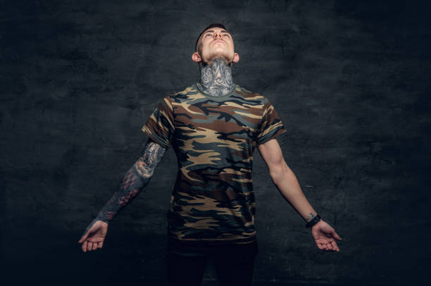 a man with tattoos on his neck, face and arms, dressed in a camouflage t shirt. - costume mustache child disguise imagens e fotografias de stock