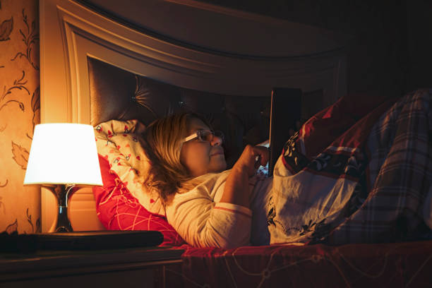 Senior woman lying in bed at night with tablet and falling sleep