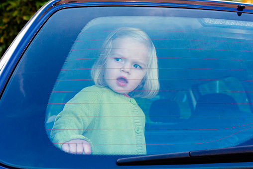 Child girl closed in the back of a car on a hot day. Concept image of danger of overheating in car for young children in the summer
