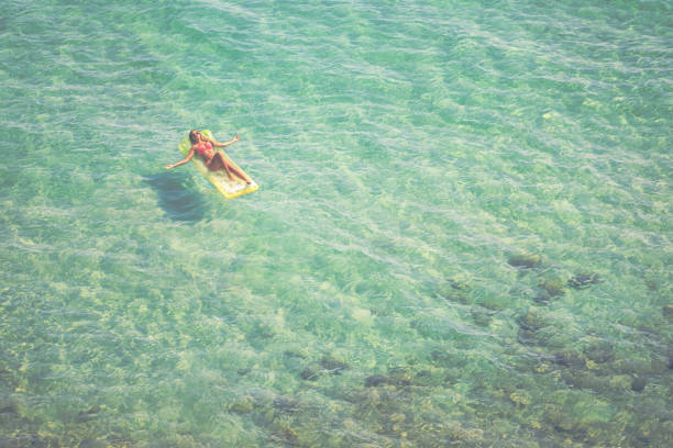Young woman relaxing at the beach while sunbathing and floating on a mattress