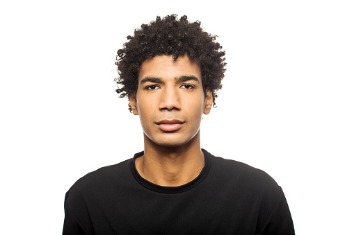 Portrait of young man against white background. Serious male is having short curly hair. He is wearing black casuals.
