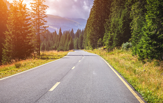 Mountain road. Landscape with rocks, sunny sky with clouds and beautiful asphalt road in the evening in summer. Vintage toning. Travel background. Highway in mountains. Transportation