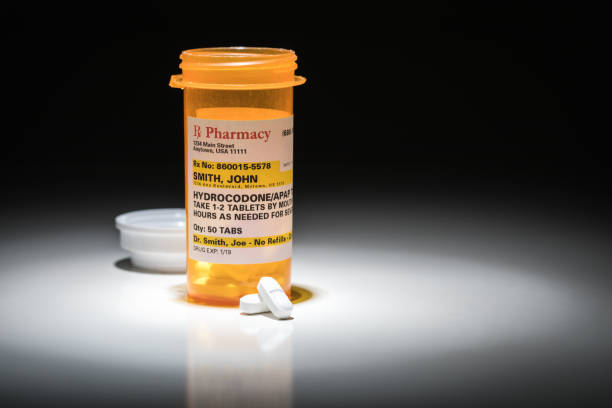 hydrocodone pills and prescription bottle with non proprietary label. no model release required - contains fictitious information. - hydrocodone imagens e fotografias de stock