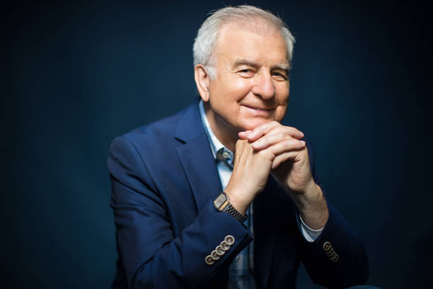 Portrait of confident smiling businessman with hands clasped. Senior man is in formalwear. He is against blue background.