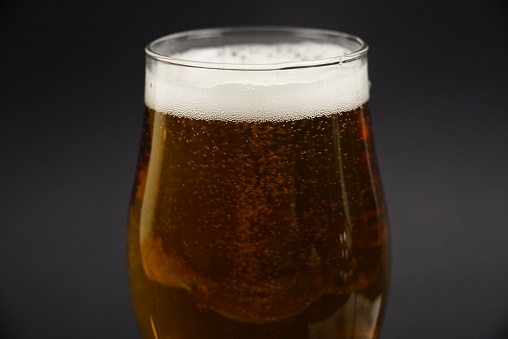 Close up shot of a foamy beer in a glass against black studio background.