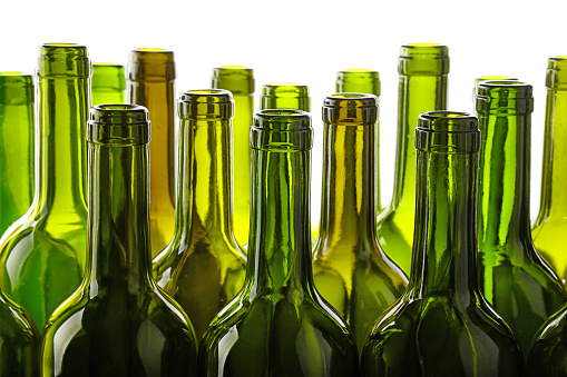 Close up group of many empty washed green glass wine bottles in a row isolated on white background, low angle side view