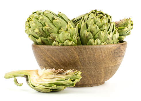 Globe artichoke set in a wooden bowl with one slice near isolated on white background raw fresh cut