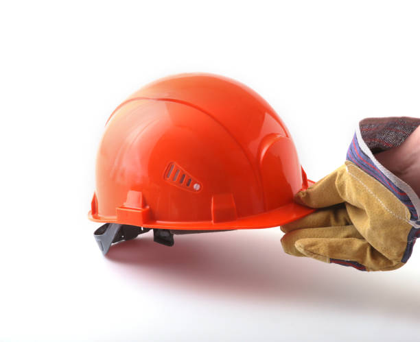 istock worker in protective gloves holds an orange hard hat in his hand. Safety helmet. 936330450