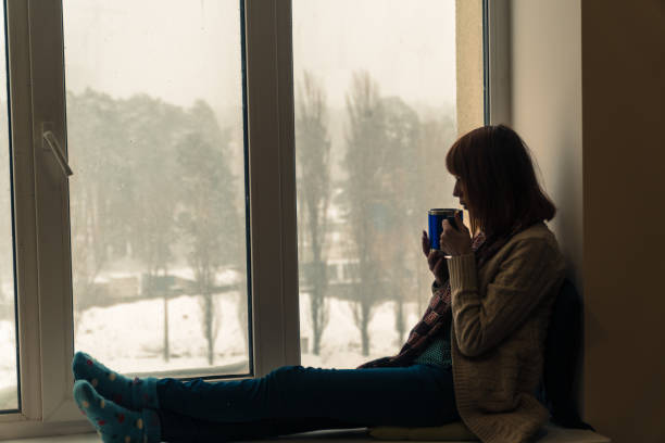 istock Winter. A girl sits on a window sill and drinks her 936331958