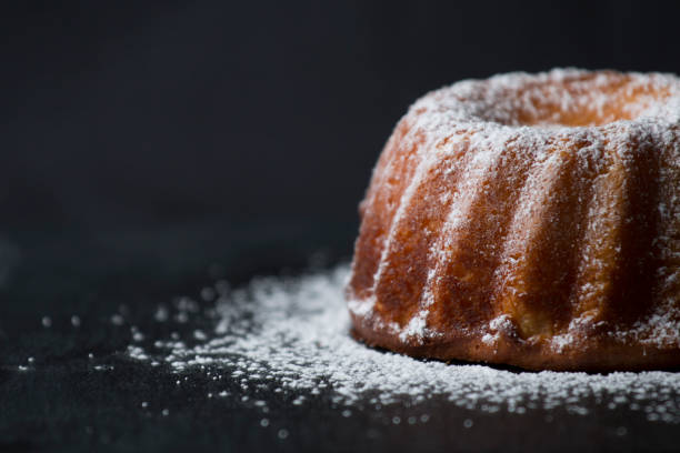 Bundt butter cake Delicious butter bundt cake sprinkled with icing sugar on a black background. pound cake stock pictures, royalty-free photos & images