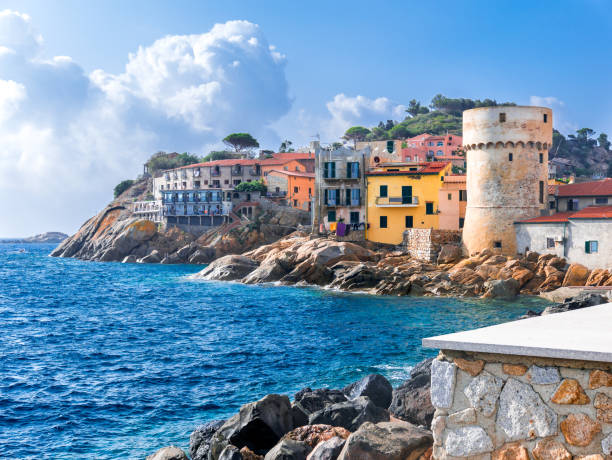 The perfect tiny seaside village of "Giglio Porto" with multi colored houses, an ancient defensive tower and a rocky coastline against a deep blue Mediterranean sea. - Giglio Island, Tuscany, Italy The perfect tiny seaside village of "Giglio Porto" with multi colored houses, an ancient defensive tower and a rocky coastline against a deep blue Mediterranean sea. - Giglio Island, Tuscany, Italy livorno stock pictures, royalty-free photos & images