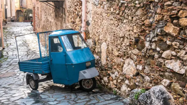 Castelmola, Taormina, Messina. March 2017: traditional vintage vehicle with three weels and blue metal paint, called Ape car,  parked on the street, next to a rural house with big stone wall.