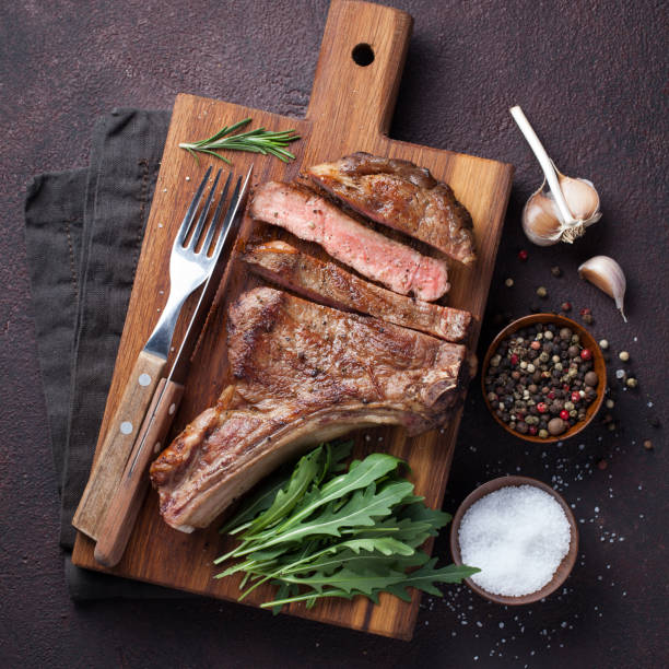 istock Grilled cowboy beef steak, herbs and spices on a dark stone background. Top view 936338482