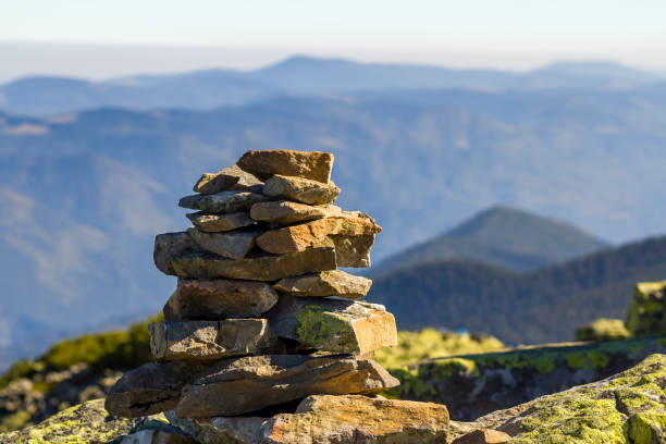 istock Stack of stones covered with moss on top of a mountain on mountains background. Concept of balance and harmony. Stack of zen rocks. Wild nature and geology detail. 936343524