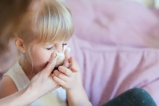 Photo of Child with runny nose. Mother helping to blow kid's nose with paper tissue. Seasonal sickness