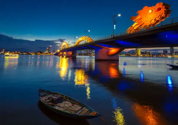 Photo of Dragon Bridge in Danang at night, with reflections on the river.