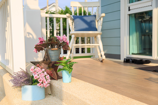 Pink flower bouquet in a blue pot and plant with a white wooden rocking chair on  wooden floor in balcony with nature and sky background.