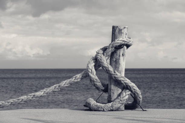 Old rope on seafront, sea and cloudy sky. Black and white toned landscape.