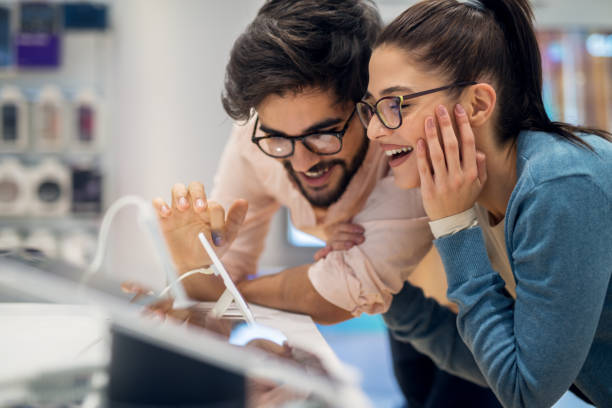 cerrar vista de pareja de amor joven muy contento emocionado hipster probar nuevos gadgets inteligentes en una tienda de tecnología. - tienda de electrónica fotografías e imágenes de stock