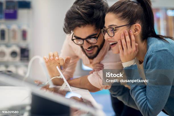 Close Up Side View Of Pretty Happy Excited Hipster Young Love Couple Testing New Smart Gadgets In A Tech Store Stock Photo - Download Image Now