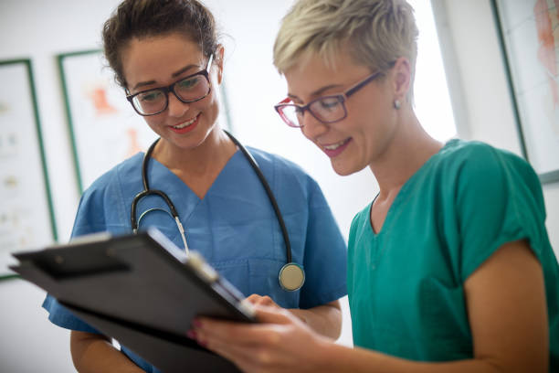 Close up of a two cheerful smiling professional female doctors with stethoscope looking at the clipboard of a patient. Close up of a two cheerful smiling professional female doctors with stethoscope looking at the clipboard of a patient. team event stock pictures, royalty-free photos & images