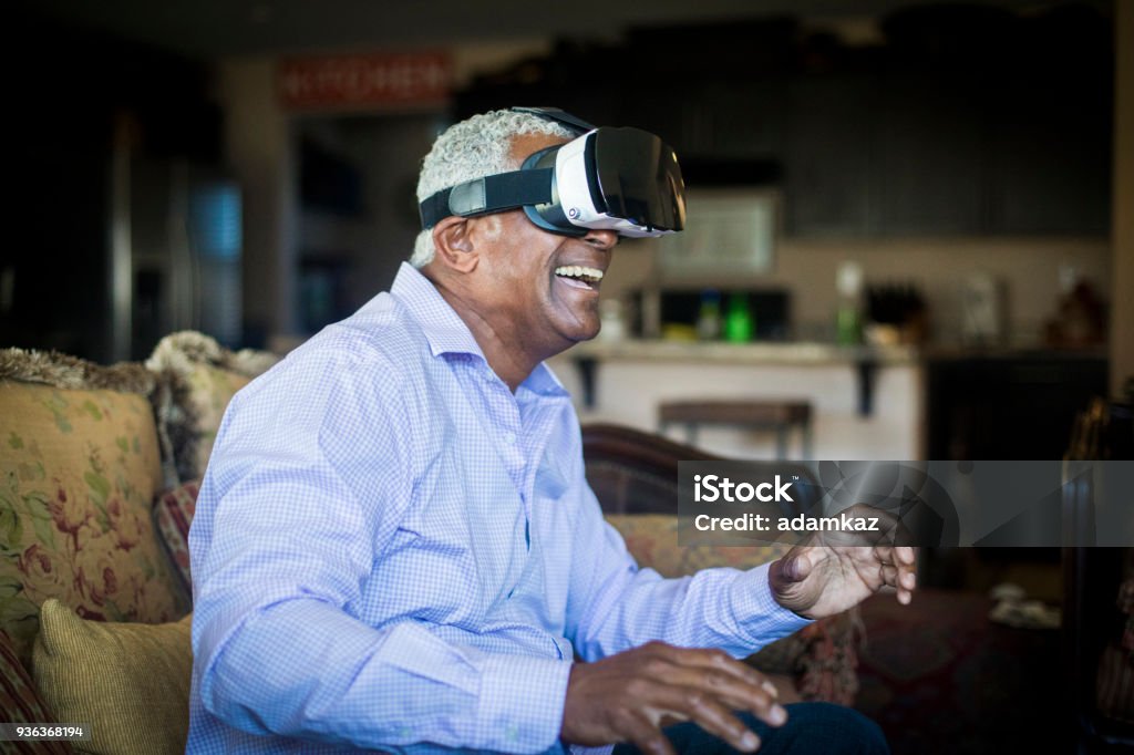 Senior Black Man Using Virtual Reality Headset in Living Room A senior black man using virtual reality headset technology in his living room Virtual Reality Simulator Stock Photo