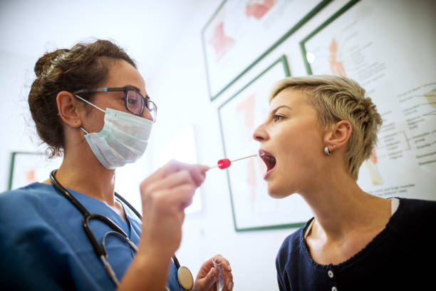 Side close view of female doctor specialist with face mask holding buccal cotton swab and test tube ready to collect DNA from the cells on the inside of a woman patient. Side close view of female doctor specialist with face mask holding buccal cotton swab and test tube ready to collect DNA from the cells on the inside of a woman patient. Saliva stock pictures, royalty-free photos & images