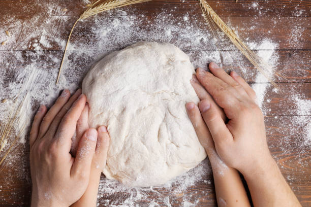 istock Homemade pastry for bread or pizza. Easter baking background. Father and child hands prepares the dough with flour on wooden table. 936373142