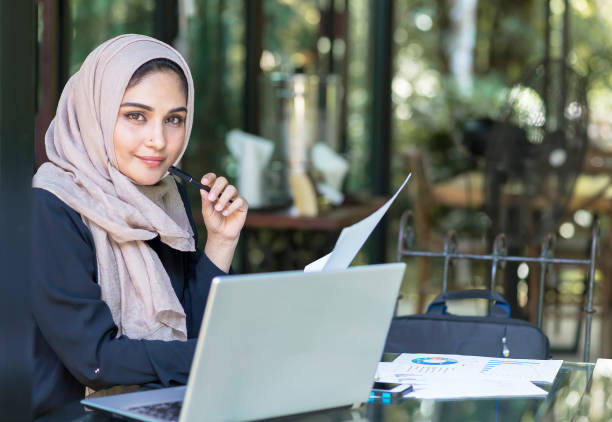 bella donna che indossa l'hijab di fronte alla ricerca di laptop e fa lavoro d'ufficio, affari, finanza e concetto di workstation. - bahrain foto e immagini stock